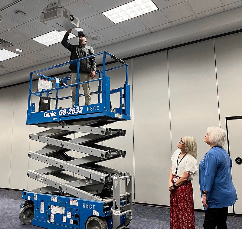 Zach Weaver, on lift, chief engineer at the Hot Springs Convention Center, adjusts one of the new laser projectors at the center while Director of Operations Jennifer Wolcott, left, and Director of Sales Tammy Clampet look on. Photo is courtesy of Visit Hot Springs. - Submitted photo