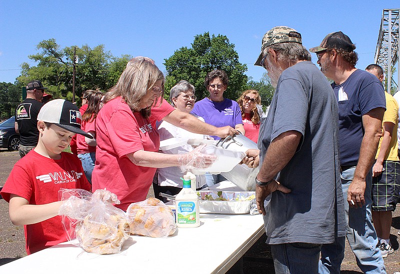 Luke Tapscott, left, prepares to hand out a roll as Yolanda Clark, second from left, hands a boxed meal to a guest during Walnut Church of Christ's meal service Sunday afternoon, April 16, 2023, in the parking lot at West Fourth and Elm streets in Texarkana, Texas. The meal consisted of beef and gravy, salad, rolls, peach cobbler, tea and water. Walnut Church of Christ hosts a devotional and the meal, part of its ministry for the homeless, from noon until the food is gone every third Sunday at the parking lot, said Brian Tapscott, Luke's father and deacon of the ministry. The 12-year-old ministry, which was spearheaded by David and Kimberly Jackson, serves food to about 100 people and also provides clothing. The food and clothing are donated by church members. Walnut's ministries include Tigers Cub Closet, which supplies hygiene and other items to children in school; and Beds for Kids, which provides a new bed for children going into foster care. Walnut Church of Christ is at 2720 Moores Lane. (Staff photo by Stevon Gamble)