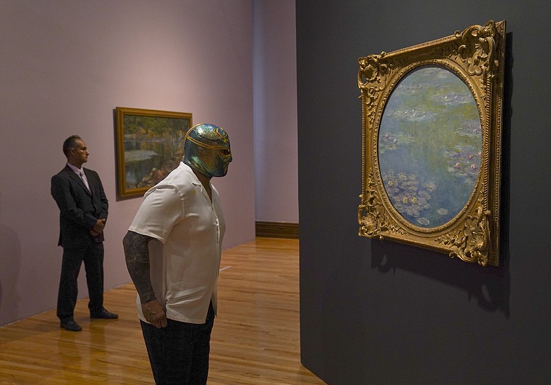 El luchador mexicano CintaDeOro observa una pintura de Claude Monet durante la inauguración de la exposición “Monet. Luces del Impresionismo” en la Ciudad de México el 26 de abril de 2023. (Foto AP/Fernando Llano)