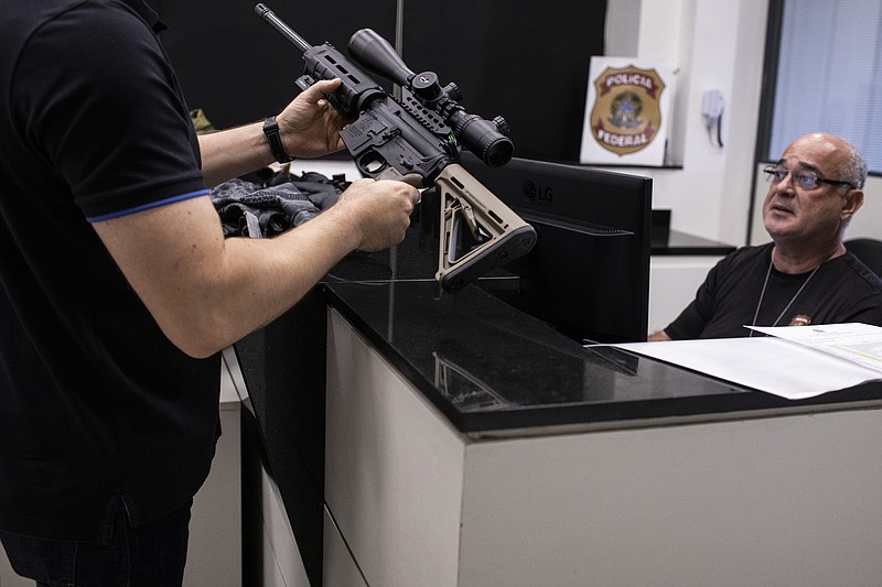 Un propietario sostiene un arma mientras un agente de la Policía Federal la registra en el Sistema Nacional de Armas, el 3 de abril de 2023, en Río de Janeiro, Brasil. (AP Foto/Bruna Prado)