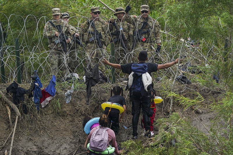 Un migrante abre los brazos frente a miembros de la Guardia Nacional de Texas ubicados detrás de alambre de púas en una de las márgenes del río Bravo, el jueves 11 de mayo de 2023, vistos desde Matamoros, México. (AP Foto/Fernando Llano)