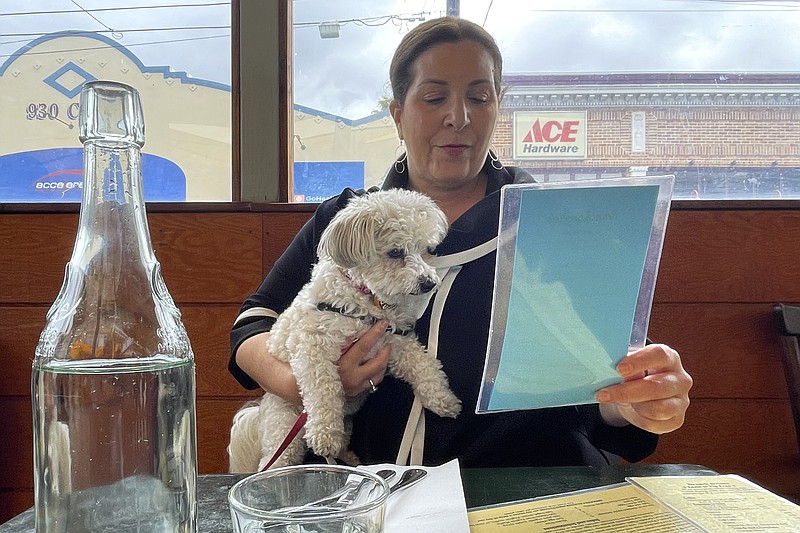Ilana Minkoff checks out the menu with her dog JoJo Wigglebutt at a restaurant in San Francisco on Friday, May 5, 2023. Just in time for the summer dining season, the U.S. government has given its blessing to restaurants that want to allow pet dogs in their outdoor spaces. (AP Photo/Haven Daley)