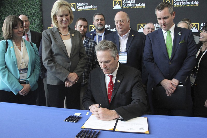 Alaska Gov. Mike Dunleavy signs legislation that would allow the state to set up a carbon offset program Tuesday, May 23, 2023, in Anchorage, Alaska. Dunleavy signed the bill with Alaska lawmakers and administration officials standing behind him during the Alaska Sustainable Energy Conference at the Dena'ina Civic and Convention Center in downtown Anchorage. (AP Photo/Mark Thiessen)