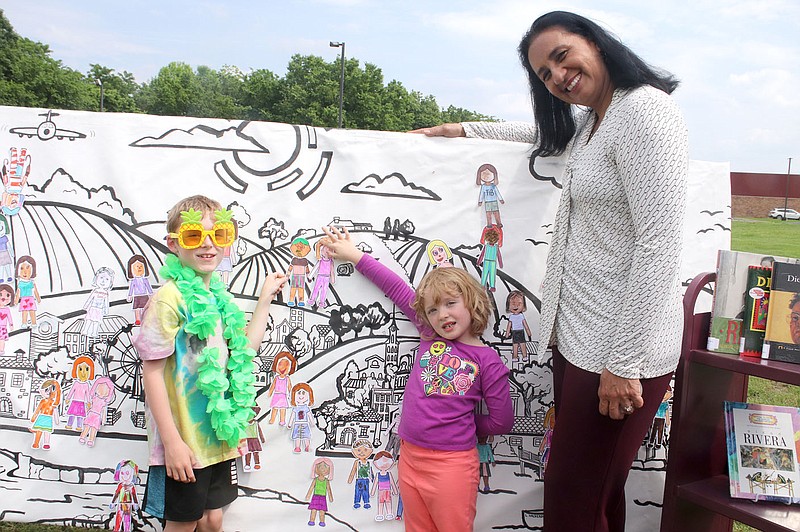 Lynn Kutter/Enterprise-Leader
Artist María de Lourdes Valverde Galindo, right, stands with Levi Plant, 7, and his sister, Mae Plant, 5, of Farmington, on Tuesday, May 23, 2023, as they point out their decorated paper dolls on a community mural for Farmington Public Library. Crystal Bridges Museum of American Art in Bentonville set up its mobile art lab last week to introduce guests to a paper doll portrait activity and community mural activity inspired by “Diego Riveras America.”  Galindo, who created the mural, was on site to help and visit with children and their parents. The theme for the summer reading program is "All Together Now."