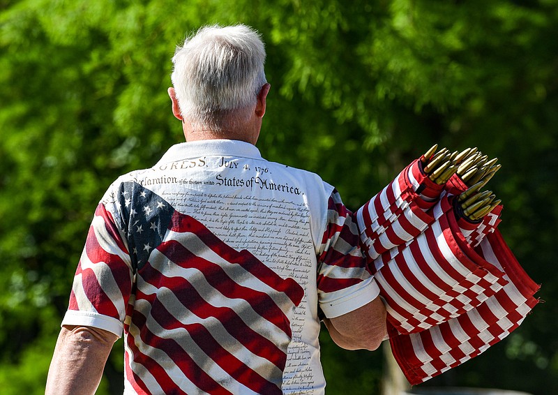 Julie Smith/News Tribune photo: 
With an armful of small American flags, volunteer Roger Schwartz makes his way to a section of Resurrection Cemetery Friday morning, May 26, 2023, where he and two dozen other volunteers placed a red, white and blue flag at each United States military veteran buried there. In all, the group put out over 800 of the flags ahead of Memorial Day.