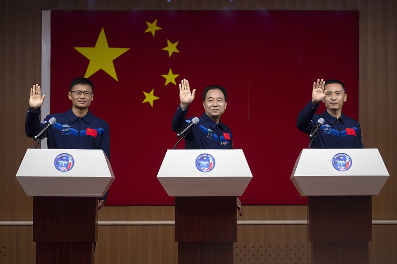 Chinese astronauts for the upcoming Shenzhou-16 mission, from left, Gui Haichao, Jing Haipeng and Zhu Yangzhu wave as they stand behind glass during a meeting with the press at the Jiuquan Satellite Launch Center on Monday, May 29, 2023, in northwest China. China's space program plans to land astronauts on the moon before 2030, a top official with the country's space program said Monday. (AP Photo/Mark Schiefelbein)