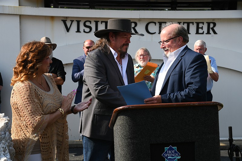 County Judge Darryl Mahoney, right, makes a presentation to country music artist Buddy Jewell Friday evening as he is inducted into the Arkansas Walk of Fame in front of the Hot Springs Visitor Center in downtown Hot Springs. Jewell later headlined a free concert in the Bridge Street Entertainment District. - Photo by Lance Brownfield of The Sentinel-Record