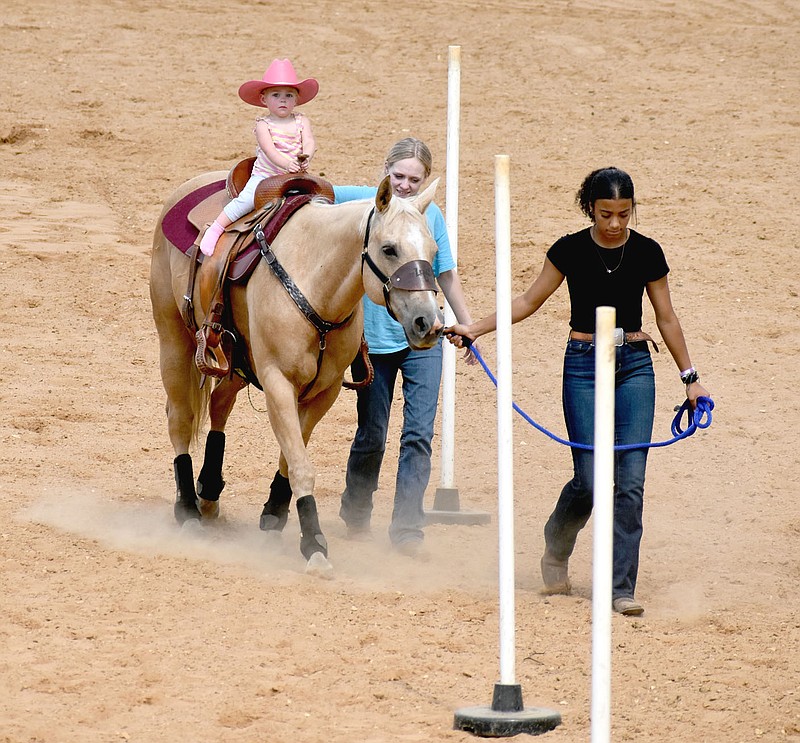 Mark Humphrey/Enterprise-Leader
Two-year-old Rae Newton sports a pink cowgirl hat while riding tall in the saddle on her way to winning the lead line pole bending competition with a time of 41.607 at the Lincoln Riding Club Play Day on Sunday. Rae's big sister, Jade Newton, a rising sophomore at Lincoln, has the lead line, while Ashton Couch walks by Rae's side making certain this fearless tiny-tot cowgirl stays in the saddle.