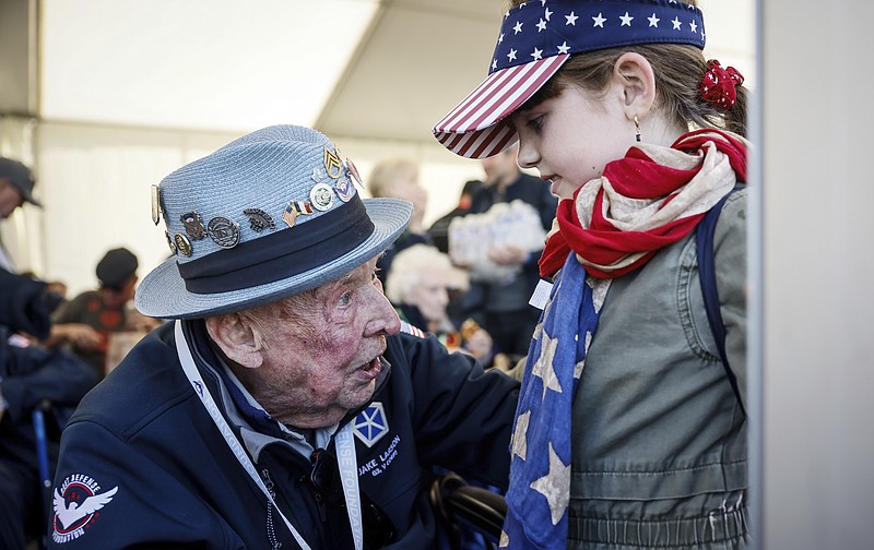 U.S. veteran SSgt. Jake M. Larson talks to a girl who wears an American flag around her neck during a gathering in preparation of the 79th D-Day anniversary in La Fiere, Normandy, France, Sunday, June 4, 2023. The landings on the coast of Normandy 79 year ago by U.S. and British troops took place on June 6, 1944. (AP Photo/Thomas Padilla)
