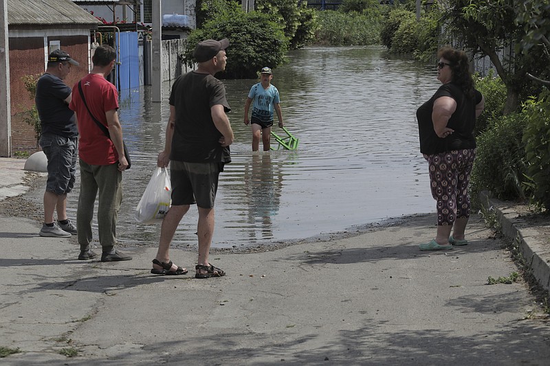 Local residents talk near their houses, which were flooded after the Russian troops blew the Kakhovka dam overnight, in Kherson, Ukraine, Tuesday, June 6, 2023. Ukraine on Tuesday accused Russian forces of blowing up a major dam and hydroelectric power station in a part of southern Ukraine that Russia controls, risking environmental disaster. (AP Photo/Nina Lyashonok)