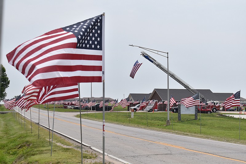 Democrat photo/Garrett Fuller — Flags line Buchanan Street on Thursday as a memorial service for John J. Lucas occurs at Windmill Ridge Funeral Service. Lucas, who was killed June 3 in a motorcycle accident in Tipton, served his community as a 911 dispatcher, jailer, CPR instructor, firefighter, emergency medical technician and ordained minister. Volunteers with The Flagman's Mission Continues, a nonprofit that honors fallen heroes, helped setup flags with local volunteers Wednesday in Lucas' honor.
