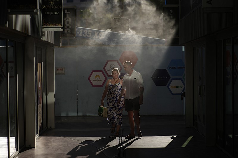 FILE - People walk through cooling misters along the Las Vegas Strip, July 13, 2023, in Las Vegas. A historic heat wave that turned the Southwest into a blast furnace throughout July is beginning to abate with the late arrival of the monsoon rains. (AP Photo/John Locher, File)
