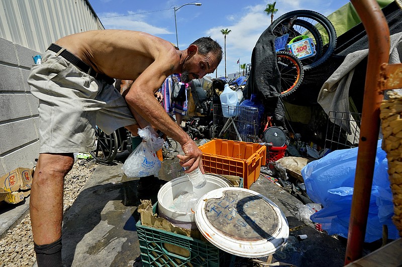 FILE - Kevin Hendershot pours ice into a bucket outside his tent in "The Zone," homeless encampment, July 14, 2023, in downtown Phoenix. Hendershot spends his days in the Justa Center, a day center for homeless people 55 years and older in the downtown area. Homeless people are among the people most likely to die in the extreme heat in metro Phoenix.  (AP Photo/Matt York, File)