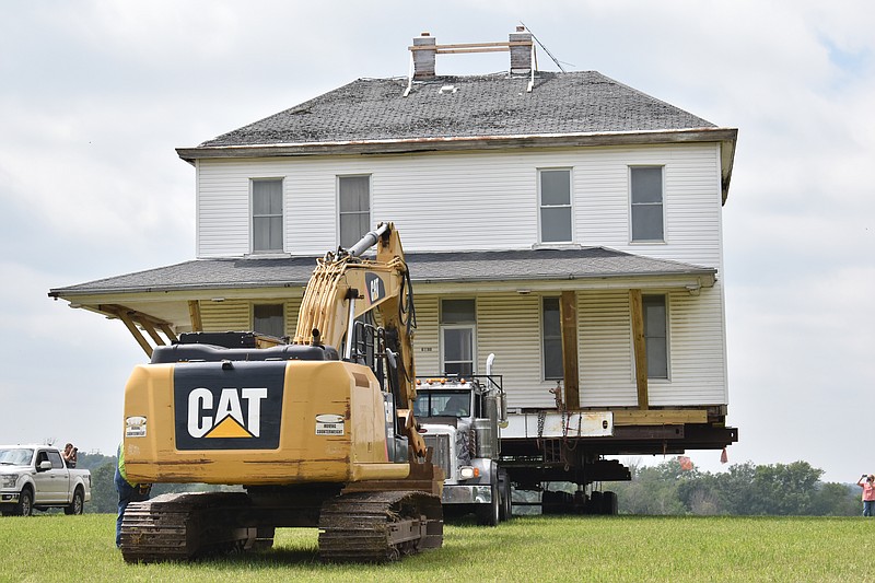 Democrat photo/Garrett Fuller — An excavator pulls a semitruck hauling a 232,000-pound home across a field Wednesday (Sept. 6) behind a row of homes in High Point. The 1860s home is being moved to a new spot closer to the High Point R-III School, where owner Steve Ramer intends to restore it for vacation rentals. Ramer grew up in the child after his family purchased it in the late 1980s. Thomas J. Hart, a Civil War captain, originally occupied the home before selling it to J.F. Tising, a prominent High Point businessman. Because of previous night's rain, the ground was soft — resulting in some minor setbacks for the Tilton and Sons House Moving crew. They had to use steel plates to prevent the truck from getting stuck, and once had to lift the house with blocks after it got stuck in a terrace.