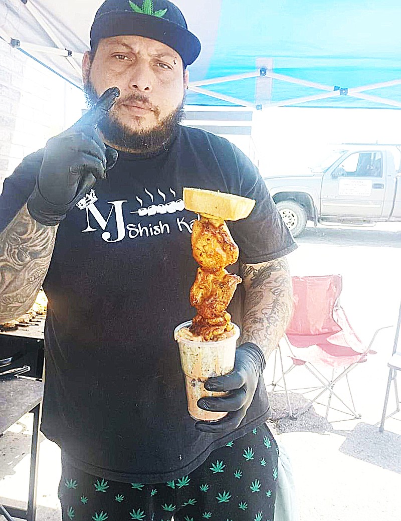 Submitted — Emmanuel Navera poses with one of his shish kabob offerings under a pop-up canopy at Mr. G's Liquor. He is moving his Puerto Rican cuisine business, MJ's Shish Kabobs & More, out of his Taylor Avenue home and into The Sweet Shoppe Café's former spot in the Eagle Stop plaza at Buchanan Street and Missouri 87.