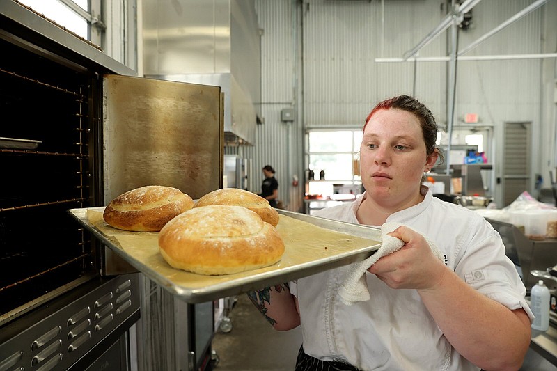 Karis Mengarelli, bakery chef at Wilson Gardens, removes freshly-baked sourdough bread from the oven in the kitchen at The Grange at Wilson Gardens in Wilson on Friday, Sept. 22, 2023. (Arkansas Democrat-Gazette/Colin Murphey)