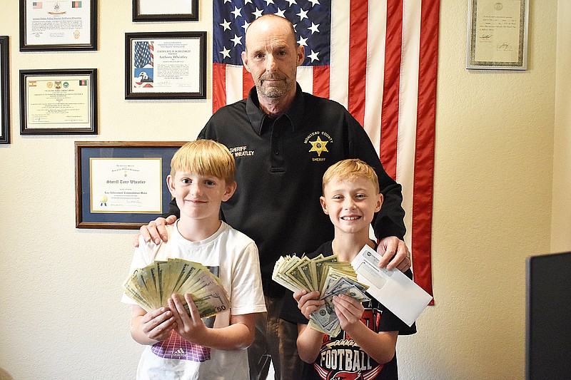 Democrat photo/Garrett Fuller — For the third year in a row, Ryder Bracht, left, and Owen Crane, right, pose with Moniteau County Sheriff Tony Wheatley with their donation Friday after fundraising for the county's Shop With A Hero program. The 9-year-old Tipton duo raised more than $2,800 through their lemonade stand for the program, which will partner underprivileged children with law enforcement officers, firefighters, emergency medical services personnel and 911 dispatchers for Christmas shopping at the Jefferson City Target. As with previous years, Bracht and Crane will attend the trip to see their efforts brighten other children's lives.