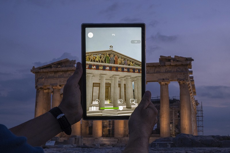 A man holds up a tablet showing a digitally overlayed virtual reconstruction of the ancient Parthenon temple, at the Acropolis Hill in Athens, Greece on Tuesday, June 13, 2023. Greece has become a late but enthusiastic convert to new technology as a way of displaying its famous archaeological monuments and deepening visitors' knowledge of ancient history. The latest virtual tour on offer is provided by a mobile app that uses Augmented Reality to produce digital overlays that show visitors at the Acropolis how the site and its sculptures looked 2,500 ago. (AP Photo/Petros Giannakouris)
