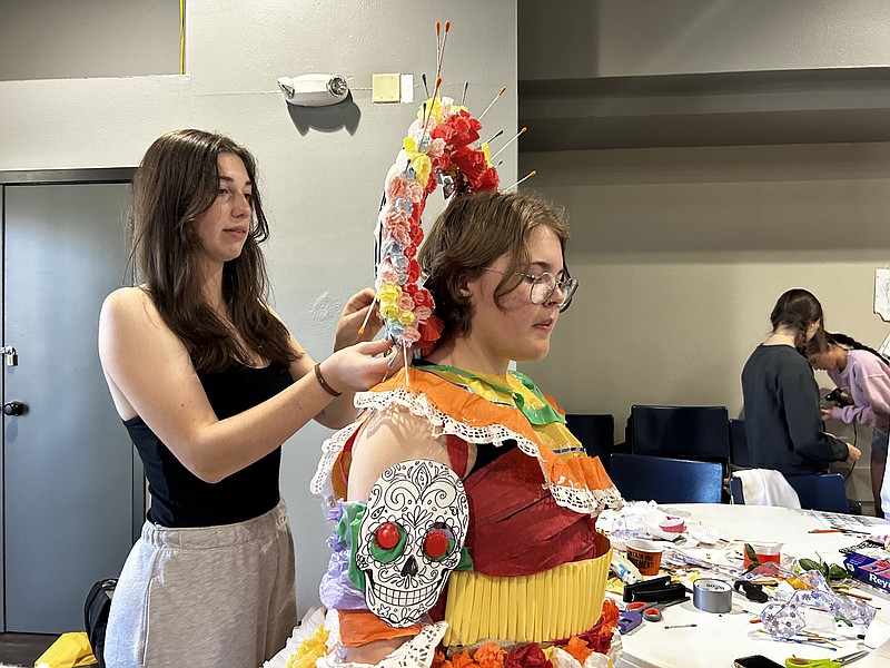 Sophomore Eden Jenable, left, puts the finishing touches on a headdress worn by sophomore Kody Franks during an art project Thursday, Oct. 19, 2023, at First Baptist Church, Moores Lane, in Texarkana, Texas. Approximately 70 art club students gathered to for a project to transform trash into works of art that were a fusion of two world cultures. (Staff photo by Sharda James)
