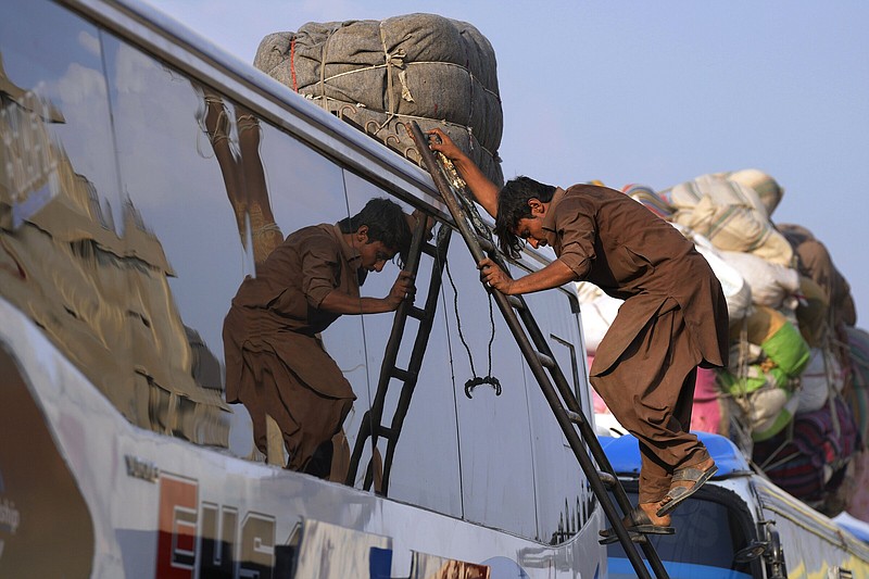 A porter climbs down after fixing luggage of an Afghan family on the rooftop of bus  Karachi, Pakistan, Tuesday, Oct. 31, 2023. Large numbers of Afghans crammed into trucks and buses in Pakistan, heading to the border to return home hours before the expiration of a Pakistani government deadline for those who are in the country illegally to leave or face deportation. (AP Photo/Fareed Khan)
