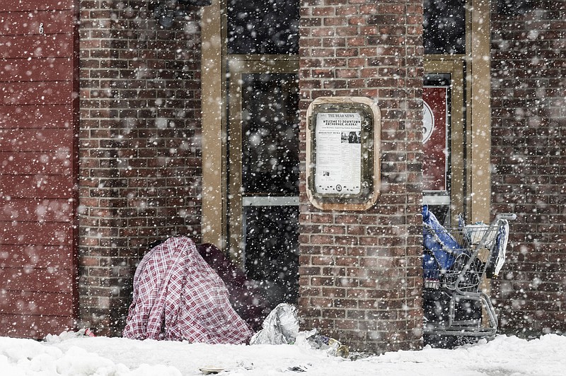 Two people take cover in an entryway of a downtown restaurant on Fourth Avenue, Thursday, Nov. 9, 2023 in Anchorage, Alaska. Four homeless people have died in Anchorage in the last week, underscoring the citys ongoing struggle to house a large houseless population at the same time winter weather has returned, with more than 2 feet (0.61 meters) of snow falling within 48 hours. (Marc Lester/Anchorage Daily News via AP)