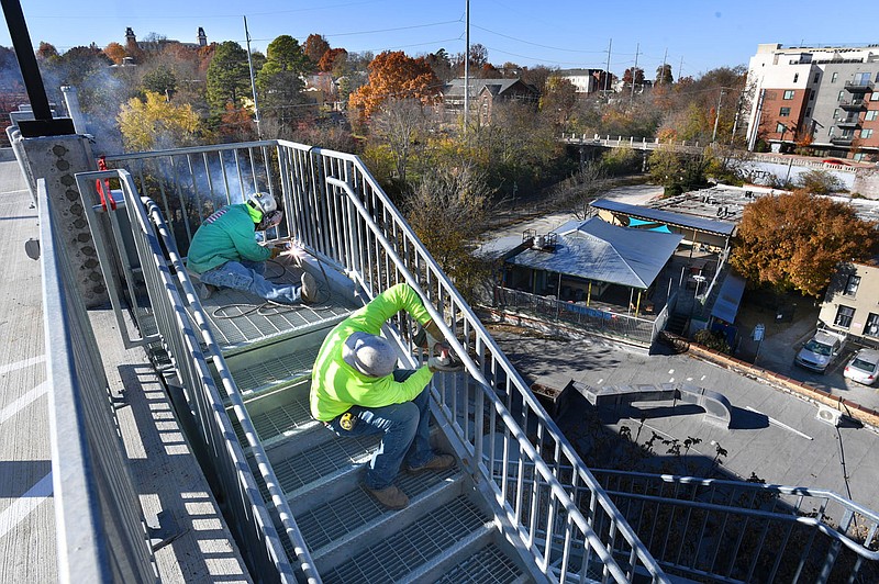 Sergio Guajardo (left) and Mauricio Gonzalez, both welder/fabricators for STI Metal Fab in Springdale, put the finishing touches Friday, Nov. 10, 2023, on a handrail on the sixth level of a newly completed parking deck in downtown Fayetteville. The new parking deck with about 300 spaces will replace the spaces lost once the parking lot west of the Walton Arts Center becomes the civic plaza of the downtown arts corridor, known as the Ramble. The Walton Arts Center lot must be vacated by 5 a.m. Monday, with construction scheduled to start that day. Visit nwaonline.com/photo for today's photo gallery.
(NWA Democrat-Gazette/Andy Shupe)