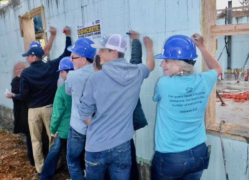 Susan Holland/Westside Eagle Observer Jennifer Peralta (right, in blue shirt) pauses briefly for a photograph as she joins her children and members of the board of Habitat for Humanity Benton County in the traditional signing of the walls of her new home. Family members, Habitat board members and other volunteers signed the home and many left encouraging messages for the family that will be living in the home.