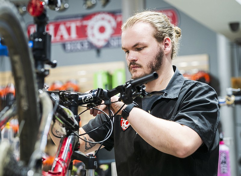 Ethan Gibbs, a bicycle mechanic with Phat Tire Bike Shop, installs brakes Friday on a bike in the shop in Bentonville. Downtown Bentonville is bringing back a program in which they give people free money to spend at local businesses downtown. Phat Tire is a participating business. Visit nwaonline.com/photos for today's photo gallery.
(NWA Democrat-Gazette/Charlie Kaijo)