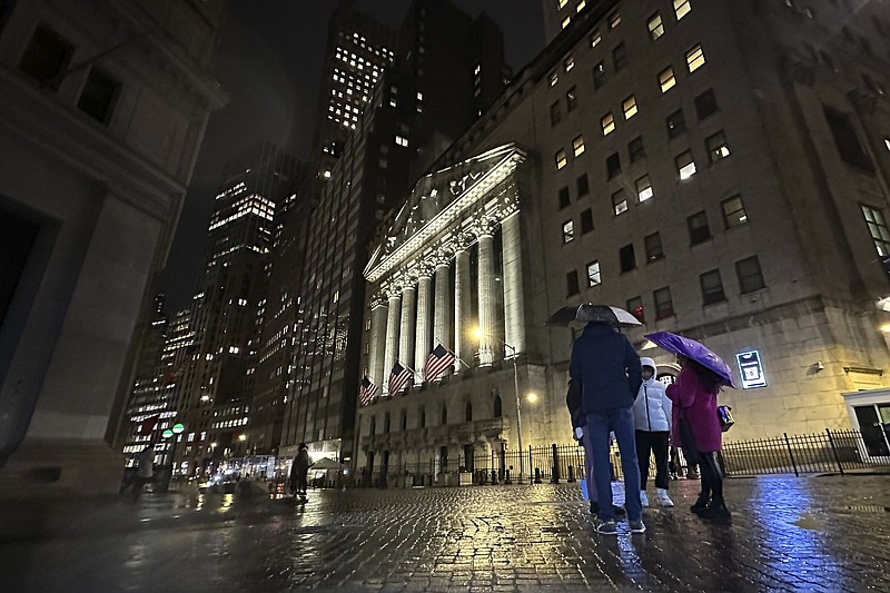 File - People huddle outside the New York Stock Exchange on Tuesday, Nov. 21, 2023 in New York. (AP Photo/Peter Morgan, File)