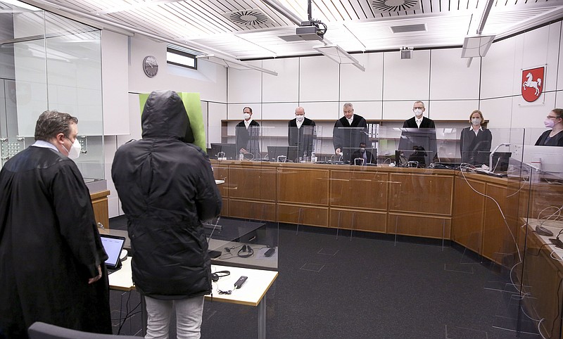 The Gambian defendant, front right, identified only as Bai L. in line with German privacy rules, holds a folder in front of his face at the Celle Higher Regional Court in Celle, Germany, Monday, April 25, 2022. The man went on trial in Germany on Monday for his alleged role in the killing of government critics in the West African country over 15 years ago. (Ronny Hartmann/Pool Photo via AP)