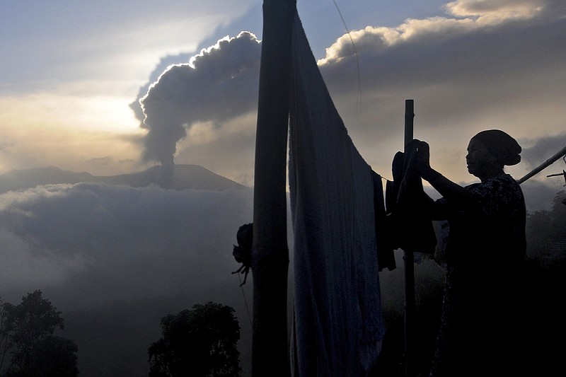 A woman hangs her laundry to dry as Mount Marapi spews volcanic ash from its crater, in Agam, West Sumatra, Indonesia, Tuesday, Dec. 5, 2023. Indonesian authorities halted Monday the search for a dozen of climbers after Mount Marapi volcano erupted again, unleashing a new burst of hot ash as high as 800 meters (2,620 feet) into the air, officials said.(AP Photo/Ardhy Fernando)
