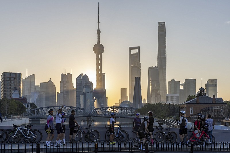 FILE - In this photo released by Xinhua News Agency, cyclists, some take selfie as they take rest against the sunrise skylines in Pudong, China's financial and commercial hub, in Shanghai, China on Friday, Nov. 3, 2023. Credit rating agency Moodys cut its outlook for Chinese sovereign bonds to negative on Tuesday, Dec. 5, 2023, citing risks from a slowing economy and a crisis in its property sector.(Wang Xiang/Xinhua via AP, File)