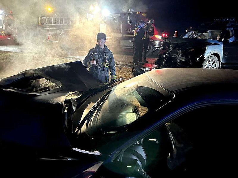 Annette Beard/Pea Ridge TIMES
Firefighter Riley Heasley measles the heat from the front of a wrecked car that had caught fire Friday night. A two-vehicle collision happened on West Pickens Road (Ark. Hwy. 94) in front of Pea Ridge High School Friday night. Pea Ridge Fire-EMS, Pea Ridge Police and Bella Vista Ambulance responded to the scene.