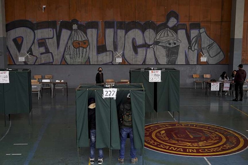 Two men vote on the draft of a new constitution in Santiago, Chile, Sunday, Dec. 17, 2023. For the second time in as many years, Chileans vote in a referendum on whether to replace the current constitution which dates back to the military dictatorship of Gen. Augusto Pinochet. (AP Photo/Matias Basualdo)