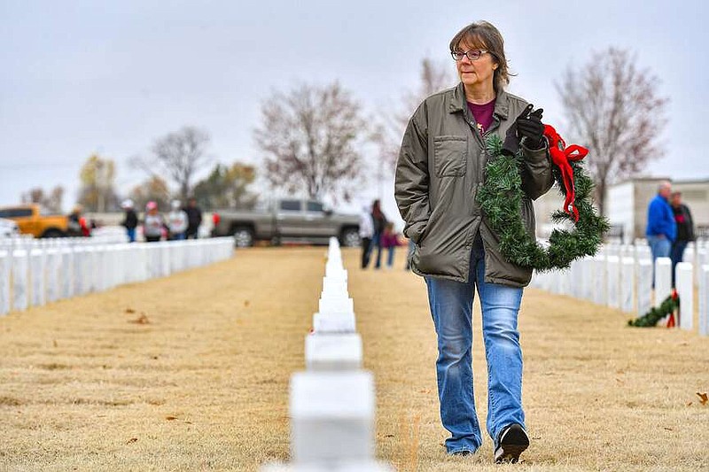 Loretta Collins of Fort Smith looks for the headstone of one of her uncles to place a wreath, Saturday, Dec. 2, 2023, during the annual Christmas Honors tradition at the Fort Smith National Cemetery in Fort Smith. Families of those buried at the cemetery were given the first opportunity Saturday morning to lay wreaths at any of its approximately 19,000 headstones. After a ceremony honoring veterans, members of the public gathered to lay the rest of the wreaths at the remaining headstones. The wreaths will remain on display until Jan. 5, 2024. Visit rivervalleydemocratgazette.com/photo for today's photo gallery.
(River Valley Democrat-Gazette/Hank Layton)