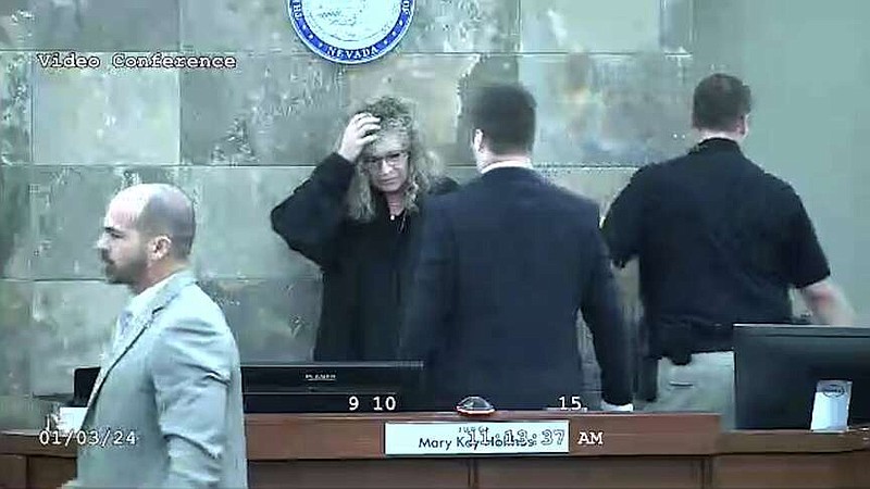 In this image from video provided by the Clark County District Court, Judge Mary Kay Holthus is seen cradling her head after a defendant launched over her desk during his sentencing in a felony battery case, Wednesday, Jan. 3, 2024 in Las Vegas. Authorities say the judge suffered minor injuries n the attack while a courtroom marshal suffered a bleeding gash on his forehead and a dislocated shoulder. (Clark County District Court via AP)
