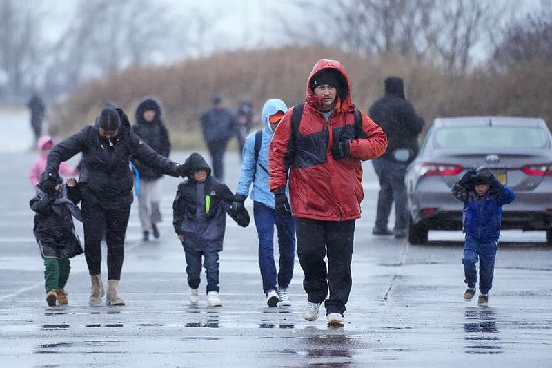 Migrantes corren bajo la lluvia hacia las carpas instaladas en el antiguo aeropuerto Floyd Bennett Field, el martes 9 de enero de 2024, en el distrito de Brooklyn en Nueva York. (AP Foto/Mary Altaffer)