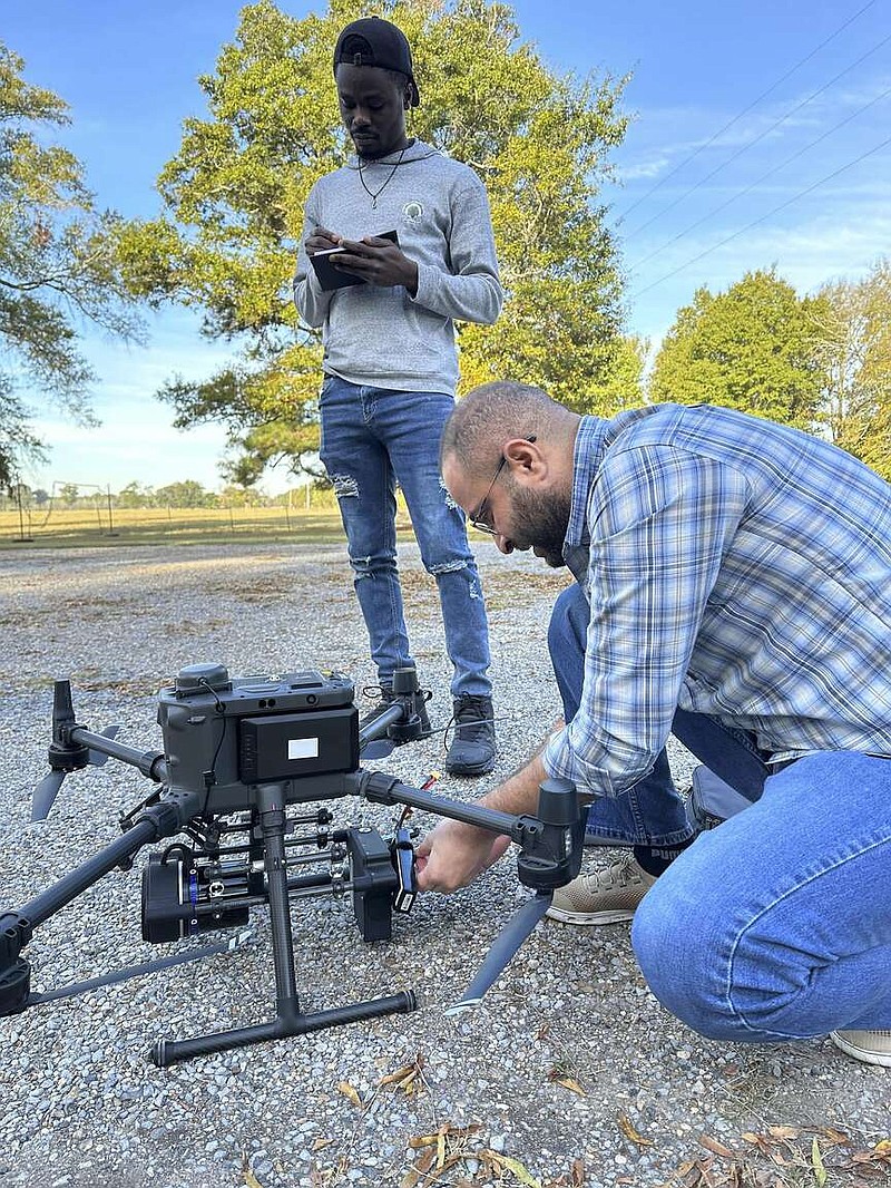 Master's student Segun 'Micheal' Adedapo stands by and records notes about the planned flight as remote sensing researcher Hamdi Zurqani prepares the drone. Adedapo is a research assistant under the supervision of Zurqani working on developing a fine-scale soil properties maps project. (Special to The Commercial/Hamdi Zurqani/University of Arkansas System Division of Agriculture)