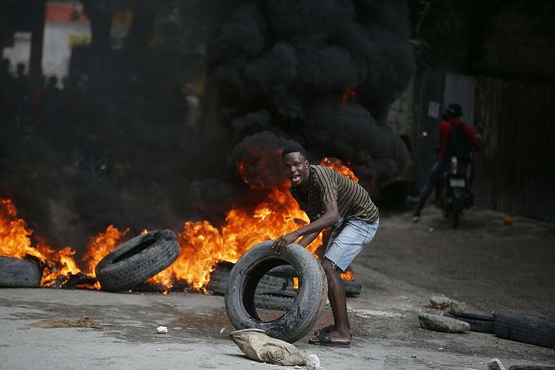 A protester adds tires to a burning barricade during a demonstration demanding the resignation of Prime Minister Ariel Henry, in Port-au-Prince, Haiti, Wednesday, Feb. 7, 2024. (AP Photo/Odelyn Joseph)