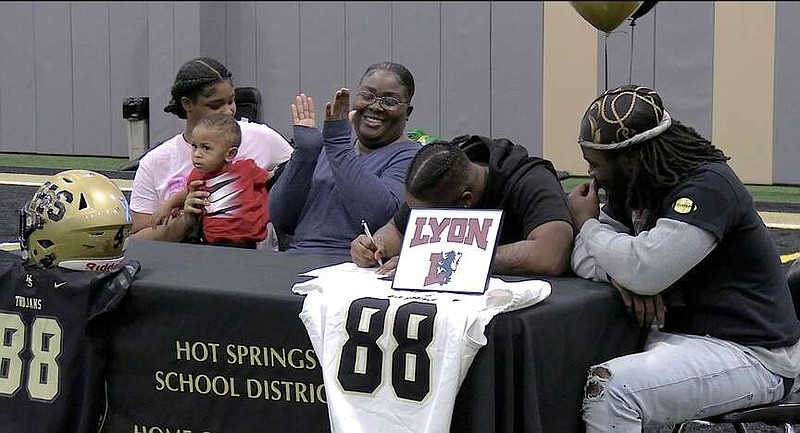 Trojans senior tight end Derrion Hawkins inks his letter of intent to play football at Lyon College on Wednesday at the Hot Springs World Class High School indoor practice facility while surrounded by family and friends. (The Sentinel-Record/Donald Cross)