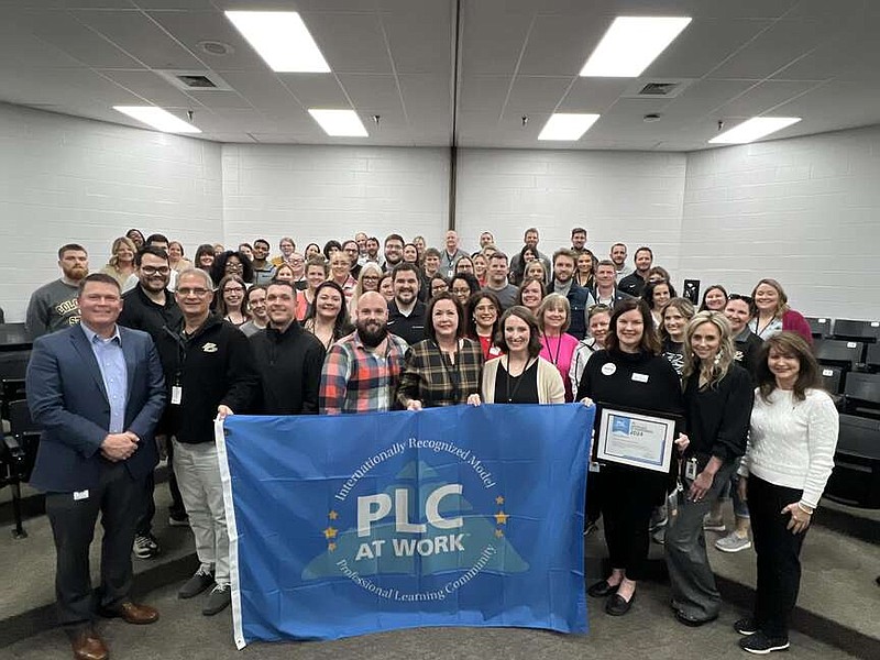Suprintendent Chad Pirtle, front left, and teachers at Pleasant Grove High School stand with a banner designating the school as a Model PLC at Work. (Photo courtesy of PGISD)