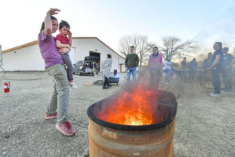 Hannah Jumper (left), a first-year doctor of osteopathic medicine student at the Arkansas Colleges of Health Education, holds her son Logan Jumper, 3, while tossing two pairs of medical scrubs into a fire pit, Monday, Feb. 19, 2024, at a ceremony on the ACHE campus in Fort Smith. Several first-year D.O. students carried on the tradition of celebrating the completion of their final anatomy course, a subject which all students at ACHE are required to take, by cheerfully burning the scrubs, shoes and other items of clothing they wore while taking the challenging courses. They also used the opportunity to make sâ€™mores, cook hotdogs and listen to music to celebrate the accomplishment. Visit rivervalleydemocratgazette.com/photo for today's photo gallery.
(River Valley Democrat-Gazette/Hank Layton)