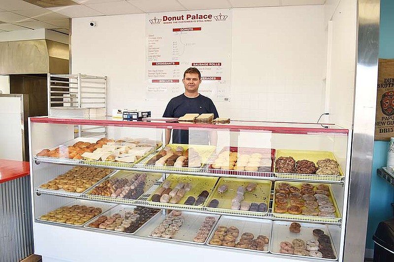 Democrat photo/Garrett Fuller — Izak Du Bruyn, owner of The Donut Palace, poses with a display case filled with doughnuts, cinnamon rolls and other pastries Feb. 26 in his new shop in the Eagle Stop Plaza at the corner of Buchanan and South Oak streets. Du Bruyn, originally from South Africa, operated another Donut Palace location in Versailles before opting for a location in a larger town.