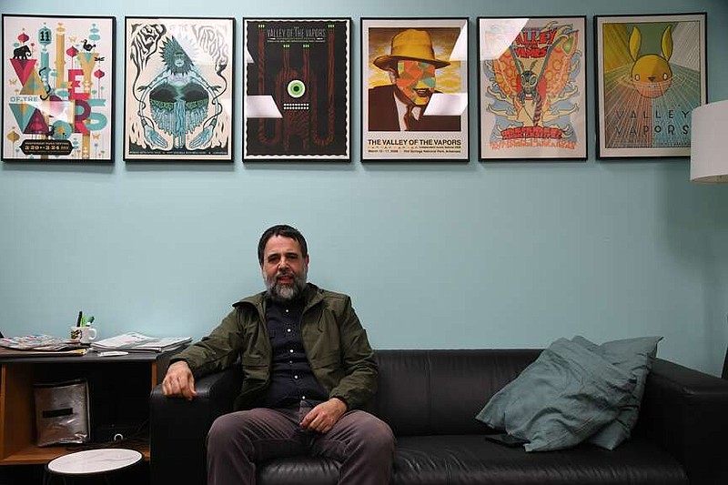 Sonny Kay, executive director of Low Key Arts, sits below a row of Valley of the Vapors posters from previous years. (The Sentinel-Record/Lance Brownfield)