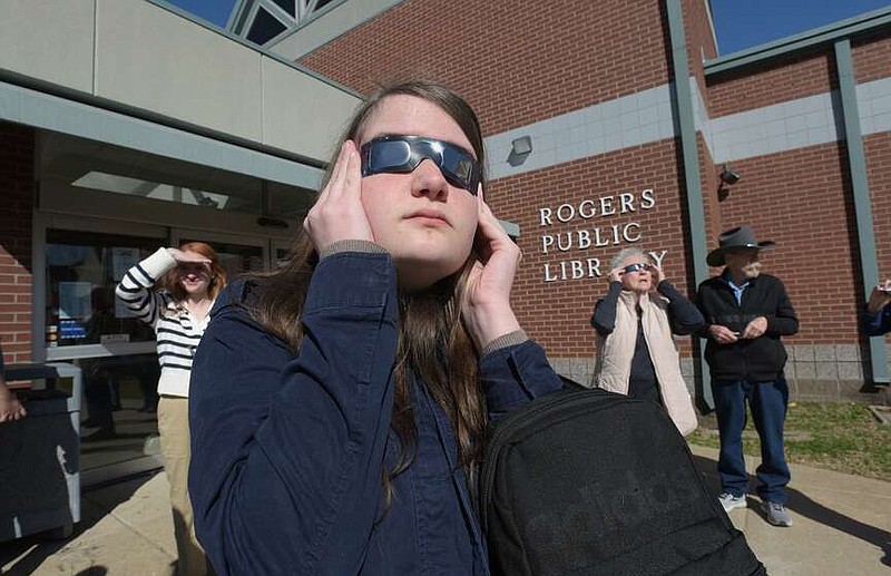 Grace Vogel joins others on Saturday, March 2 2024 for a look at the sun through safe solar eclipse glasses during an eclipse program at the Rogers Public Library. (NWA Democrat-Gazette/Flip Putthoff)