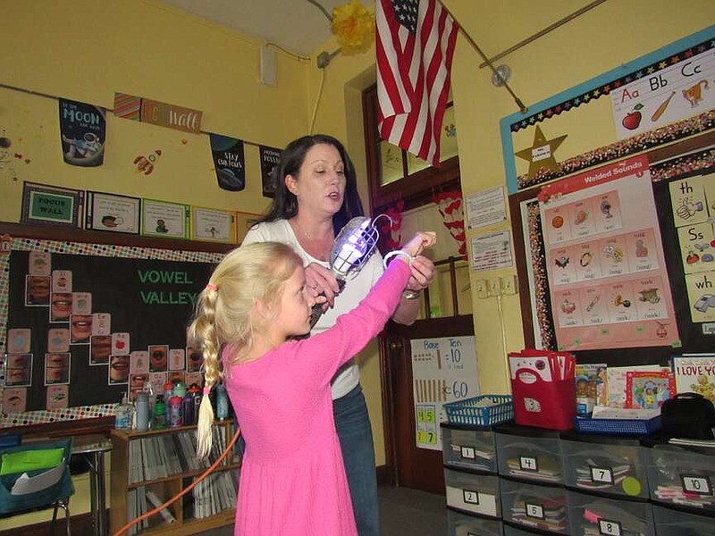 Hannah Vogler, executive director of the Arkansas STEM Coalition, shines a blacklight on the bracelet of UV beads her daughter, Evelyn, made in her class at Pulaski Heights Elementary. The beads change color when exposed to ultraviolet rays, which will be blocked by the moon during the total eclipse on Monday, April 8. 
(Arkansas Demcrat-Gazette/Kimberly Dishongh)