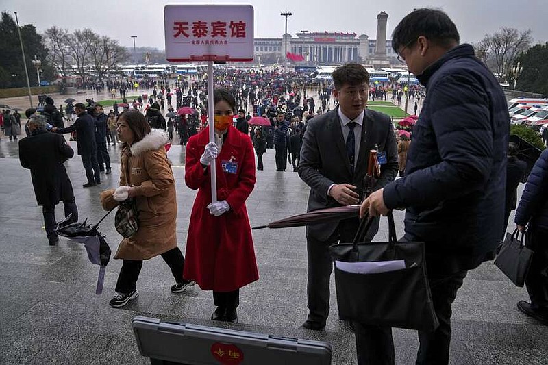 A worker distributes umbrellas to delegates as they leave the Great Hall of the People after attending the opening session of the National People's Congress (NPC) in Beijing, Tuesday, March 5, 2024. China's official growth target for this year is around 5%, Premier Li Qiang said Tuesday in an annual report on the government's plans and performance that prioritized both security and the economy. (AP Photo/Andy Wong)