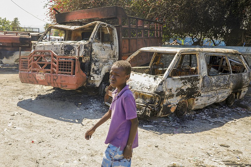 A youth walks by charred cars outside a police station set on fire by armed gangs in Port-au-Prince, Haiti, Tuesday, March 5, 2024. Prime Minister Ariel Henry has been absent since the country's latest and most serious outbreak of violence started the previous week, and armed groups have seized on the power void. (AP Photo/Odelyn Joseph)
