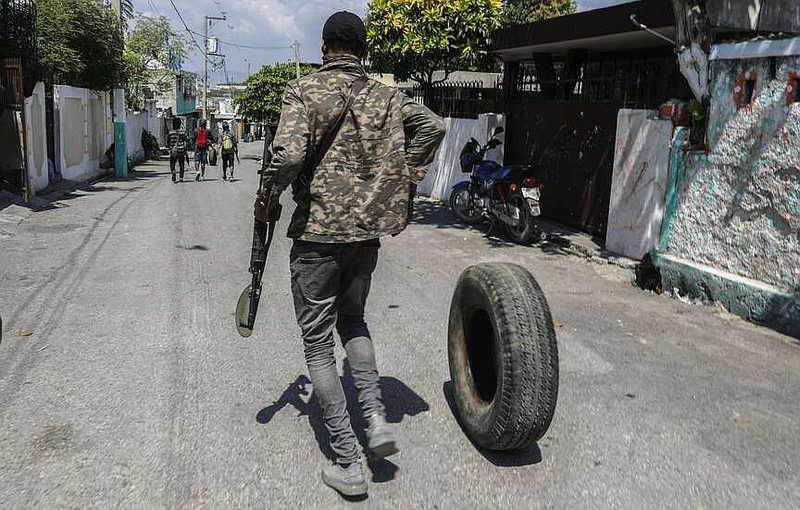 An armed member of the G9 and Family gang rolls a tire to burn at a roadblock in the Delmas 6 neighborhood of Port-au-Prince, Haiti, Monday, March 11, 2024. (AP Photo/Odelyn Joseph)