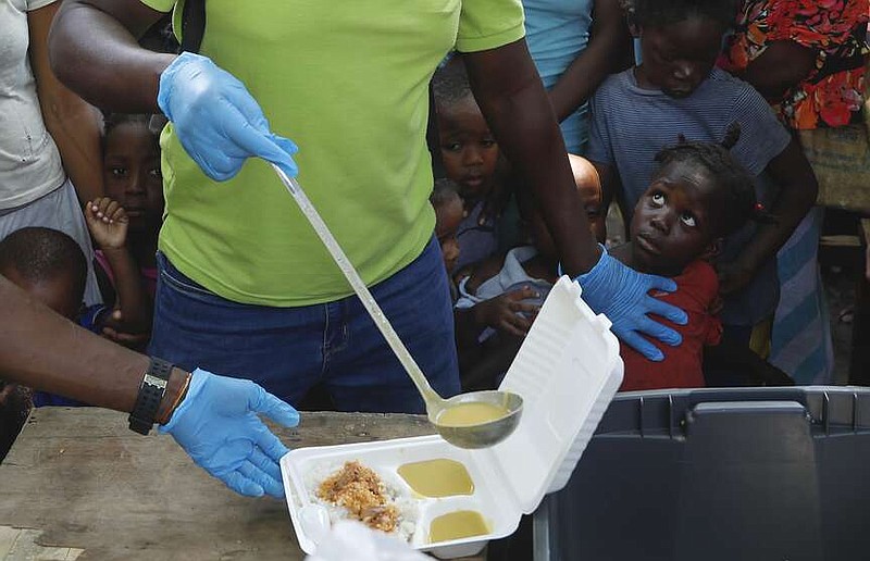 A server ladles soup into a container as children line up to receive food at a shelter for families displaced by gang violence, in Port-au-Prince, Haiti, Thursday, March 14, 2024. (AP Photo/Odelyn Joseph)